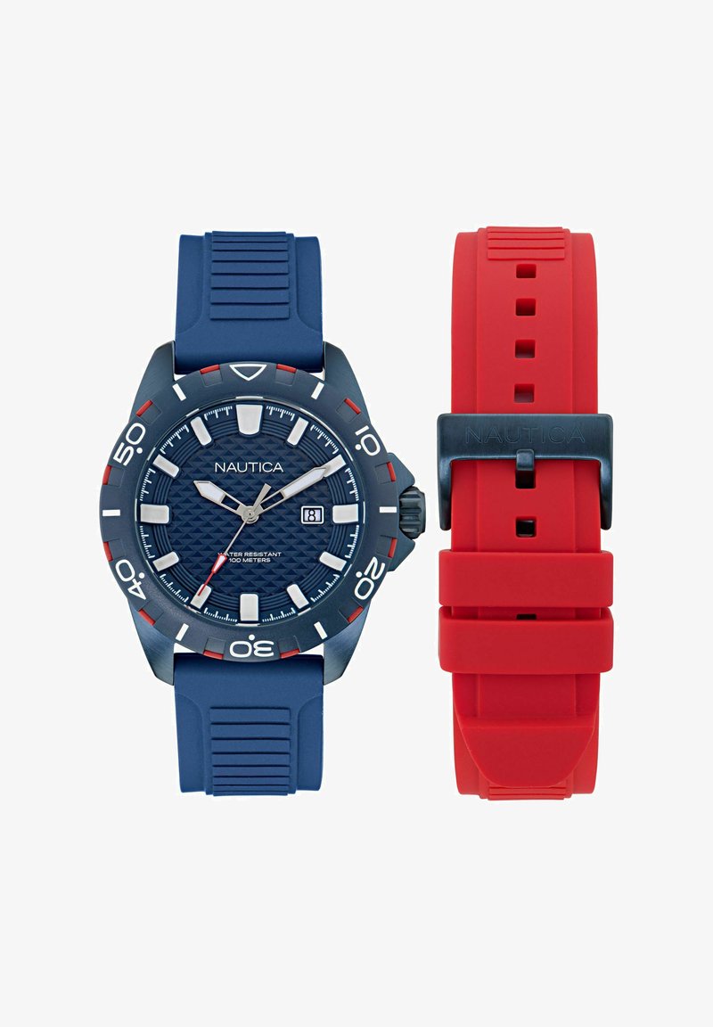 Nautica pulkstenis ar zilu silikona siksnu, strukturētu tumši zilu ciparnīcu, sudraba stundu marķieriem un sarkaniem akcentiem. Iekļauta sarkana maināmā siksna.