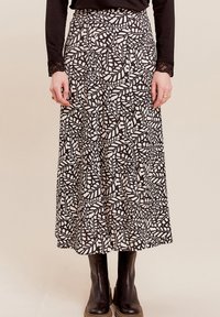 Maxi-Rock mit einem schwarz-weißen Blättermuster, aus leichtem Stoff, mit einer taillierten Taille und fließender Silhouette. Getragen mit schwarzen Stiefeln.