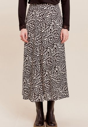 Gonna maxi con un motivo a foglie in bianco e nero, realizzata in tessuto leggero, con vita aderente e silhouette fluida. Indossata con stivali neri.
