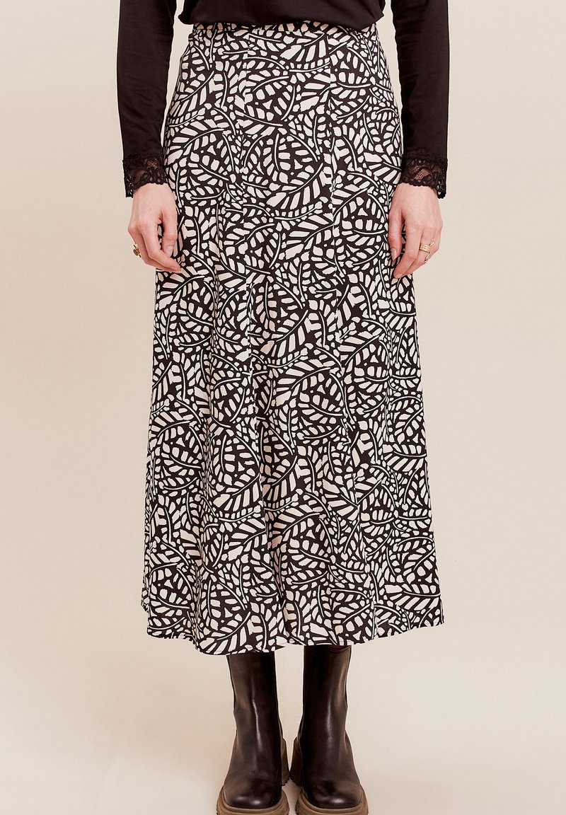 Maxi-Rock mit einem schwarz-weißen Blättermuster, aus leichtem Stoff, mit einer taillierten Taille und fließender Silhouette. Getragen mit schwarzen Stiefeln.