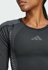 Maglietta atletica nera a maniche lunghe con un design testurizzato, strisce diagonali grigie sulle spalle e un piccolo logo sul petto.