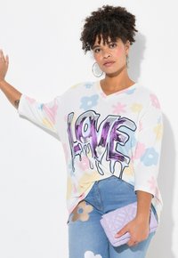 Bluza z grafiką w pastelowy wzór kwiatowy, z dużym napisem "LOVE" w fioletowym i srebrnym kolorze, połączona z jasnoniebieskimi dżinsami z kwiatowymi akcentami oraz lawendową torebką.
