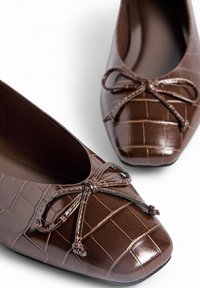 Ballerines en simili cuir marron avec une texture crocodile, bout rond et accents de nœud à l'avant. Doublure intérieure lisse.