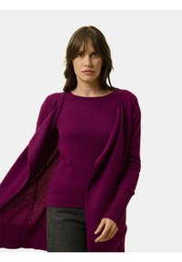 Dlouhý rukáv, otevřená cardigan v živé fialové barvě, pletená textura, s fitted vnitřní vrstvou, nošená přes sladěný top.