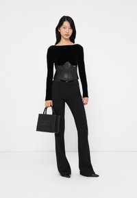 Black velvet long-sleeve top with a leather corset and padded bust, paired with black fitted trousers and a studded black handbag.