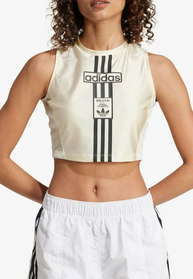 Canotta tagliata in crema con logo adidas nero, caratterizzata da tre strisce verticali e dettagli in rete sui lati.