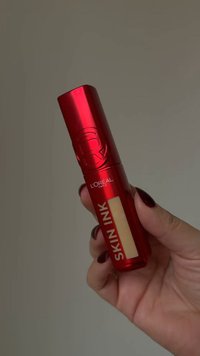 Tubo metallico rosso con finitura lucida, etichettato "SKIN INK", con una finestra trasparente che mostra il prodotto di colore chiaro all'interno.