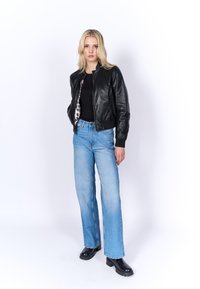 Giacca bomber in pelle nera, jeans a gamba larga blu chiaro e stivali chunky neri. La giacca è dotata di una chiusura a zip frontale e foderata in stampa leopardata.