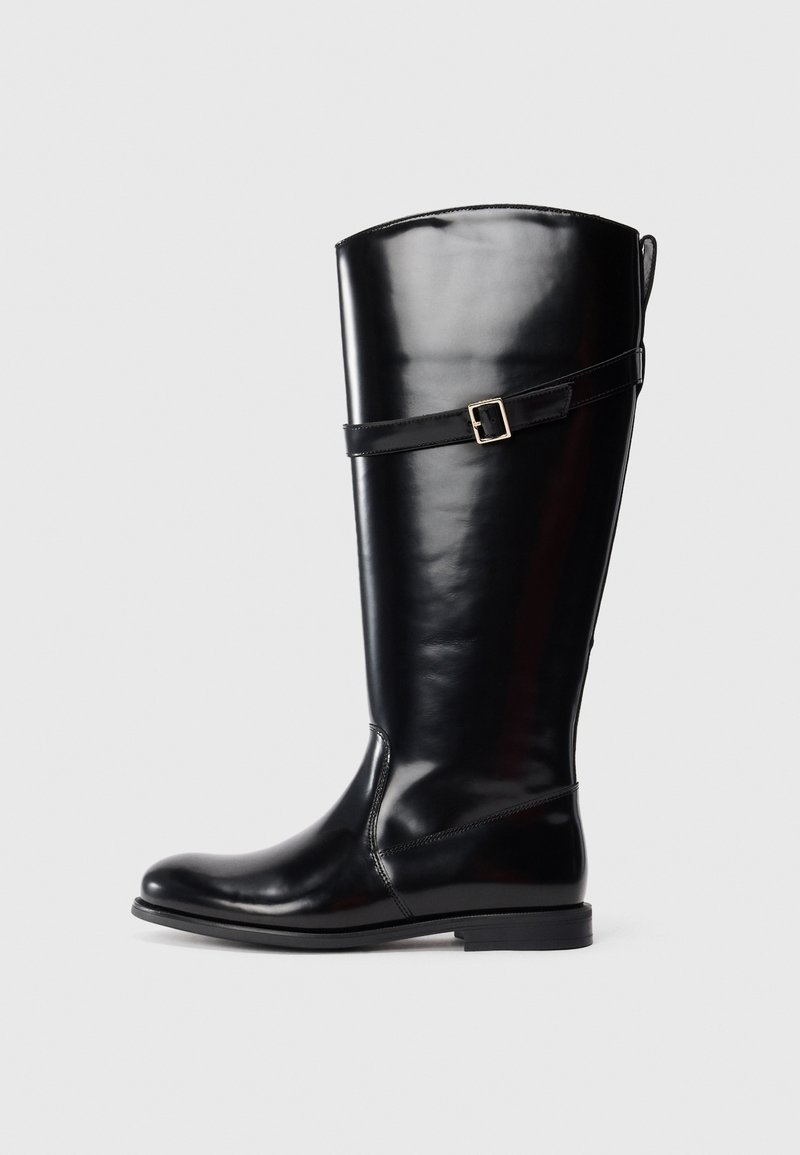 Tall black leather boot with low heel and decorative strap with silver buckle around the upper calf.