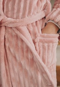 Roosa sametisest vannirobe vertikaalsete triipudega, sobiva vöö ja küljetaskuga. Pehme tekstuur ja hubane, soe välimus.