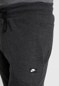 Mörkgrå Nike sweatpants med dragkedja i midjan, sidofickor och en liten svart logotyp på framsidan. Svalt, strukturerat tyg.