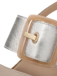 Close-up of beige sandal strap featuring a large square beige buckle with a metallic silver leather insert and gold pin.