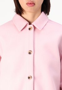 Light pink fleece jacket featuring a collar, six button closures with shiny round accents, and a textured fabric finish.