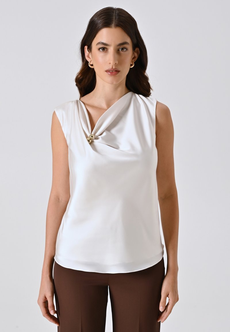Blusa bianca senza maniche con scollo drappeggiato, caratterizzata da un dettaglio a nodo impreziosito da una piccola accentatura dorata. Tessuto morbido e leggero.