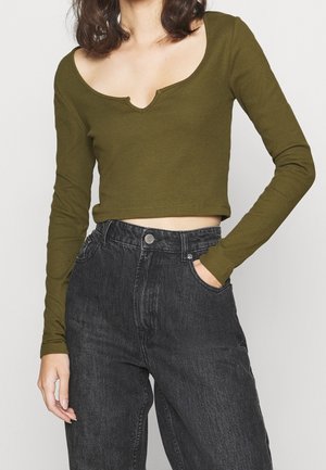 Top cropped a maniche lunghe verde oliva con scollo tondo, abbinato a jeans in denim neri a vita alta con tasche frontali visibili.