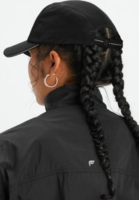 Black cap with a structured peak, paired with a lightweight black jacket. Features two braided hair sections and a silver hoop earring.
