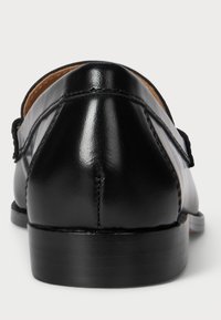 Čierne kožené mokasíny s hladkým, lesklým povrchom. Nízky podpätok a šitie pozdĺž okrajov. Žiadne viditeľné kovania ani vzory.