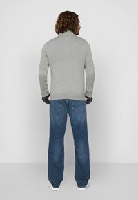 Pulover gri cu guler înalt, mâneci lungi și mansete ajustate, asociat cu blugi largi albaștri și adidași albi. Mânușile negre pun în evidență ținuta.