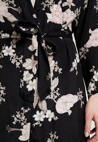 Sort blomster-indpakket kjole med lyserød og cremefarvet blomsterbroderi, et bundet taljebælte og lange ærmer med V-hals.