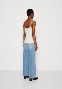 Canotta grigia chiaro con spalline sottili, abbinata a jeans a gamba larga blu. L'outfit presenta una texture liscia e una vestibilità comoda. Stivaletti neri alla caviglia.