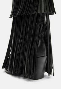 Črne črne čevlje z visokimi petami z dolgimi usnjenimi resicami. Teksturni zgornji del, z naloženim peto in gladkim zaključkom zadaj.