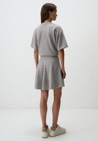 Grijze gebreide top met korte mouwen, gecombineerd met een bijpassende uitlopende rok. De outfit heeft een zachte textuur en een aansluitende taille. Casual sneakers.