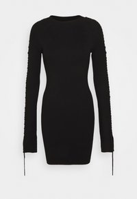 Robe noire côtelée avec manches longues, présentant un laçage latéral sur les bras. Coupe ajustée, encolure ronde et longueur mi-cuisse. Texture douce.