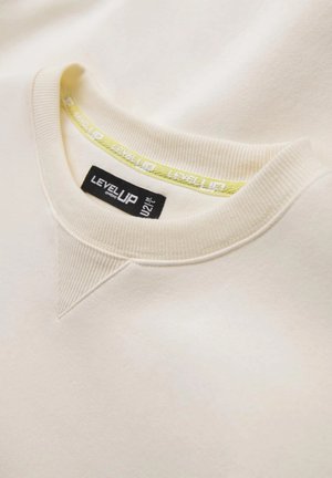 Sweatshirt beige avec un col côtelé, présentant une accent jaune avec la marque "LEVEL UP" imprimée. Texture douce, design minimaliste.