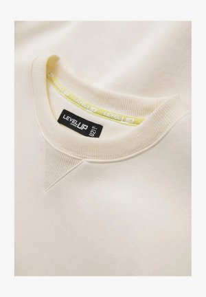 Sweatshirt beige avec un col côtelé, présentant une accent jaune avec la marque "LEVEL UP" imprimée. Texture douce, design minimaliste.