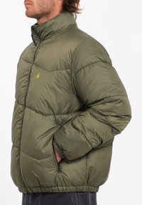 Olijfgroene pufferjack met een hoge kraag, ritszakken en een horizontaal quiltpatroon. Gemaakt van lichtgewicht, glanzend materiaal.