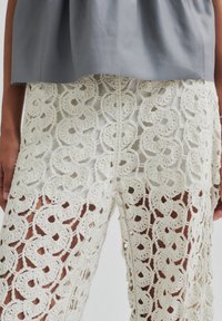Top grigio chiaro con orlo arrotondato, abbinato a pantaloni in cotone lavorati all'uncinetto di colore avorio, caratterizzati da un motivo floreale dettagliato e una trama a rete aperta.
