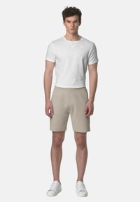 Maglietta bianca a maniche corte con scollo rotondo, abbinata a pantaloni beige e scarpe da ginnastica bianche. Abbigliamento semplice e casual con un design aderente.