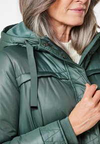Grüne Pufferjacke mit glänzender, glatter Textur, einem gesteppte Muster auf der Vorderseite und einer Kapuze mit Zugkordel und silbernen Hardware-Akzenten.