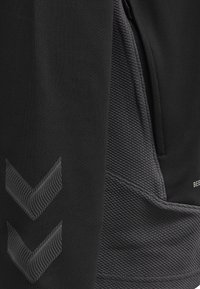 Nahaufnahme von schwarzem Stoff mit strukturiertem grauem Paneel, Doppel-Chevron-Muster und Reißverschlusstaschenkante bei Sportbekleidung.