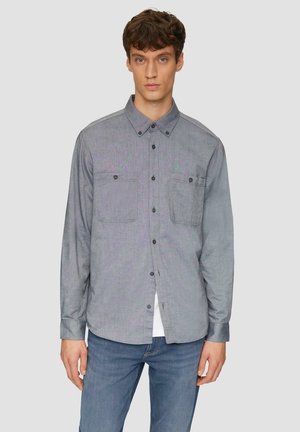Grijze button-up shirt met twee borstzakken, gemaakt van een gestructureerde stof. Lange mouwen en een klassieke kraag, gecombineerd met blauwe denim jeans.