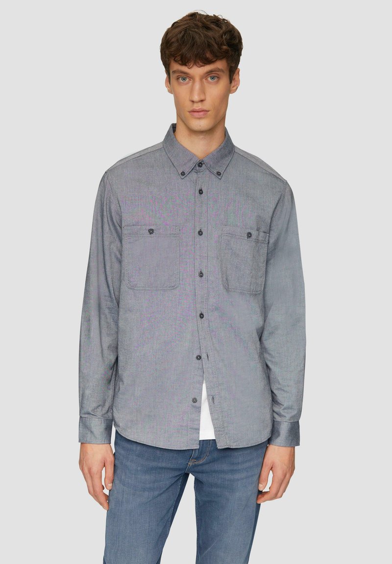 Grijze button-up shirt met twee borstzakken, gemaakt van een gestructureerde stof. Lange mouwen en een klassieke kraag, gecombineerd met blauwe denim jeans.