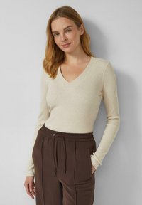 Beiger, gerippter Langarmshirt mit V-Ausschnitt, kombiniert mit dunkelbraunen Hosen mit elastischem Bund, Seitentaschen und Kordelzugverschluss.