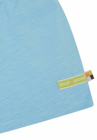 Maglietta in cotone azzurro chiaro con una texture liscia, dotata di un'etichetta verde e accenti multicolori sul lato.