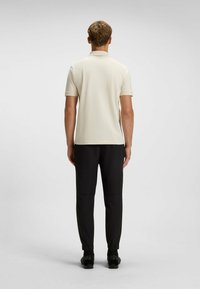 Beige Poloshirt mit kurzen Ärmeln, kombiniert mit schwarzen schmal geschnittenen Hosen. Der Stoff wirkt glatt, und das Design ist minimalistisch mit einem Kragen.