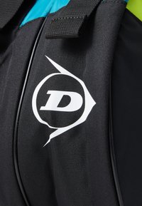 Schwarzer Stoff-Rucksack mit einem auffälligen weißen Logo in kreisförmigem Design. Strukturierte Oberfläche und Farbakzente in Türkis und Grün.