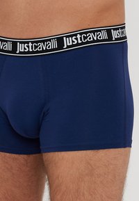 Boxeri de culoare bleumarin închis, confecționați dintr-un material moale, având o talie neagră cu text alb "Just Cavalli". Design strâns, cu o textură netedă.
