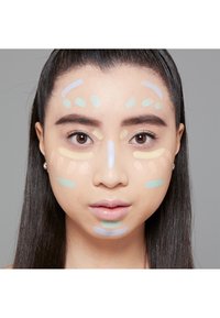 Visage avec des reflets de crème de différentes couleurs : jaune clair, vert menthe et lavande appliqués en motifs sur le front et les joues. Texture lisse.
