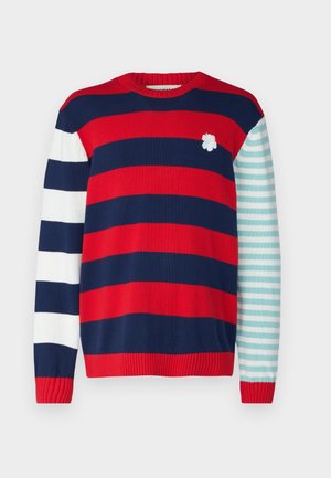 Jersey de punto con rayas horizontales rojas, azul marino y blancas; una manga presenta rayas en verde azulado y blanco. Adorno floral en el pecho.