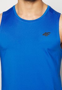 Hombre vestido con una camiseta atlética sin mangas de un brillante color azul, con un logo negro "4F" en el lado izquierdo del pecho, contra un fondo liso.