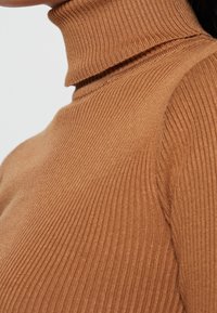 Maglione a collo alto marrone a costine con una silhouette attillata e una consistenza morbida, caratterizzato da un collo alto e una costruzione senza cuciture.