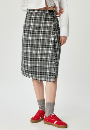 Zwart-wit geruite midi-rok met een rafelige zoom, zijdelingse sluiting en een textuurstof. Gepaard met rode sneakers en grijze sokken.