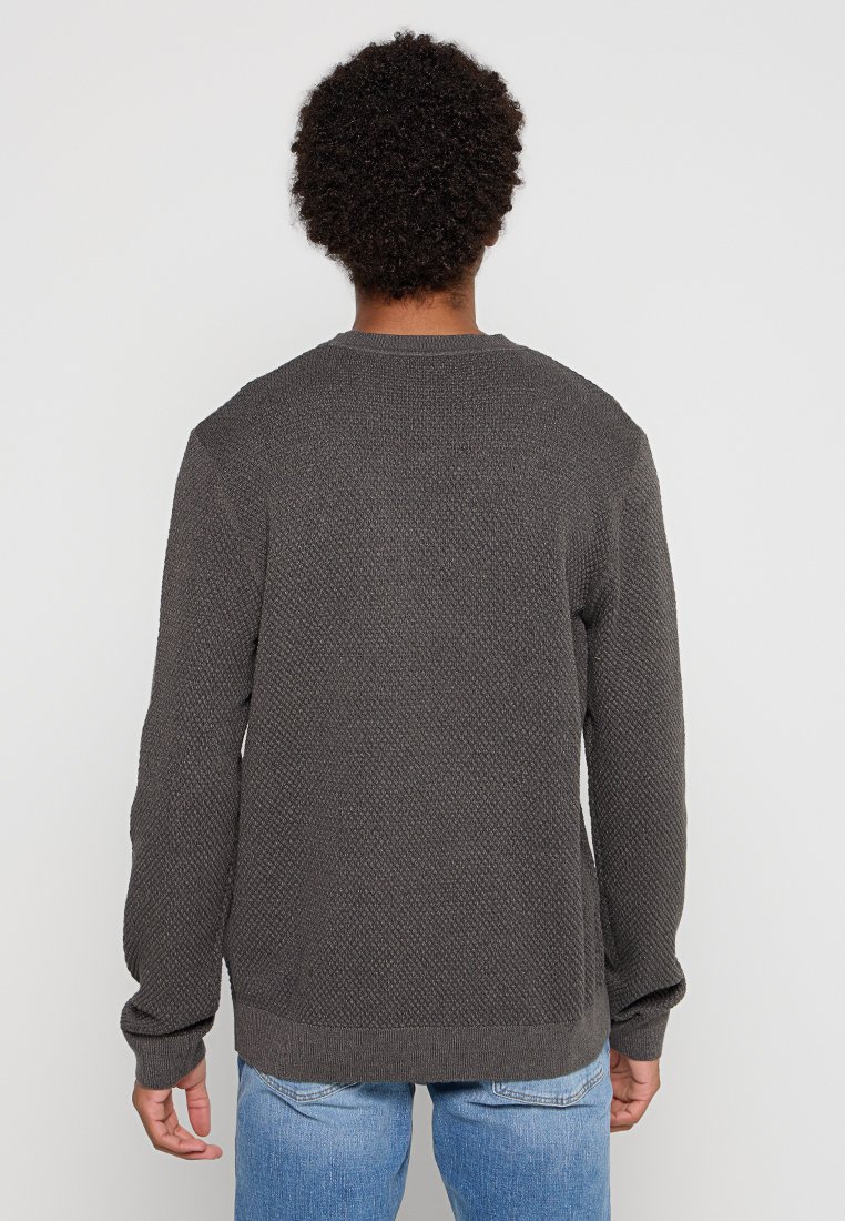 Suéter gris oscuro con un diseño de punto texturizado, cuello redondo y mangas largas, combinado con jeans de denim azul claro.