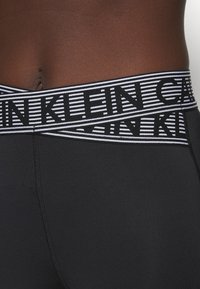 Zwarte stretchondergoed met een brede elastische tailleband met afwisselend zwarte en witte strepen en het "CALVIN KLEIN" logo in vetgedrukte letters.