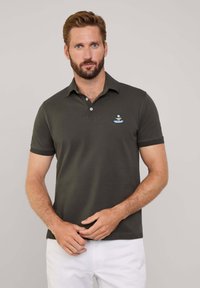 Ciemnozielona koszulka polo z krótkimi rękawami, z dwoma guzikami przy kołnierzy, z haftowanym logo na piersi. Gładka bawełniana tkanina.