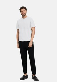 Jasnoszary T-shirt z krótkim rękawem i poziomym szwem, w połączeniu z dopasowanymi czarnymi spodniami i czarnymi butami, na jednolitym tle.